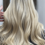 A person with long, wavy blonde hair is seen from the back, indoors.